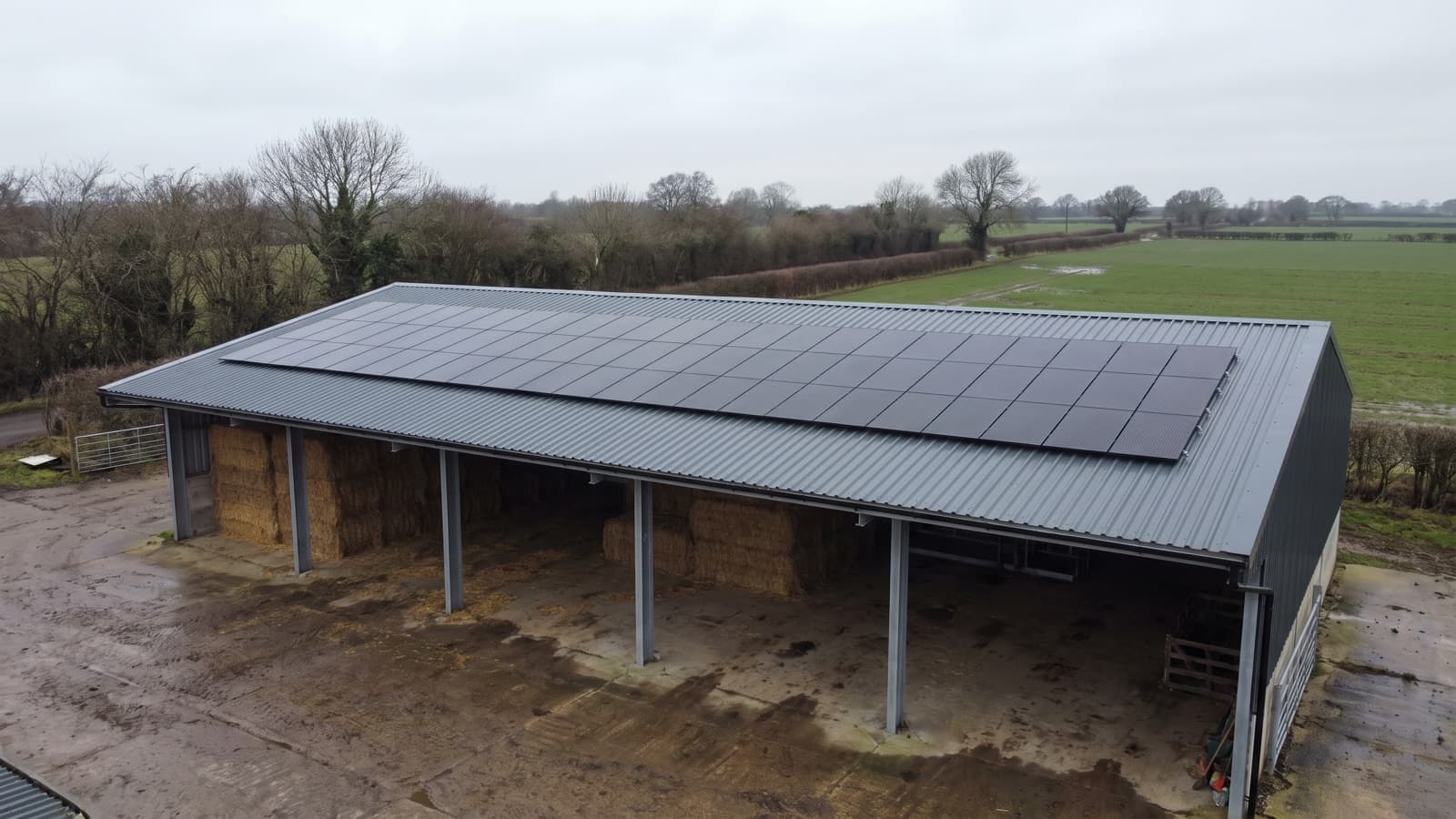 A steel portal-frame farm barn with solar panels flush-mounted in rows across its pitched steel roof.