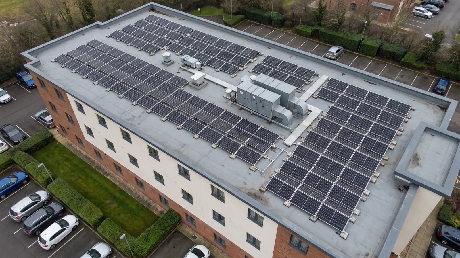 Aerial view of a roadside hotel with a ballasted solar array in rows across its flat roof.